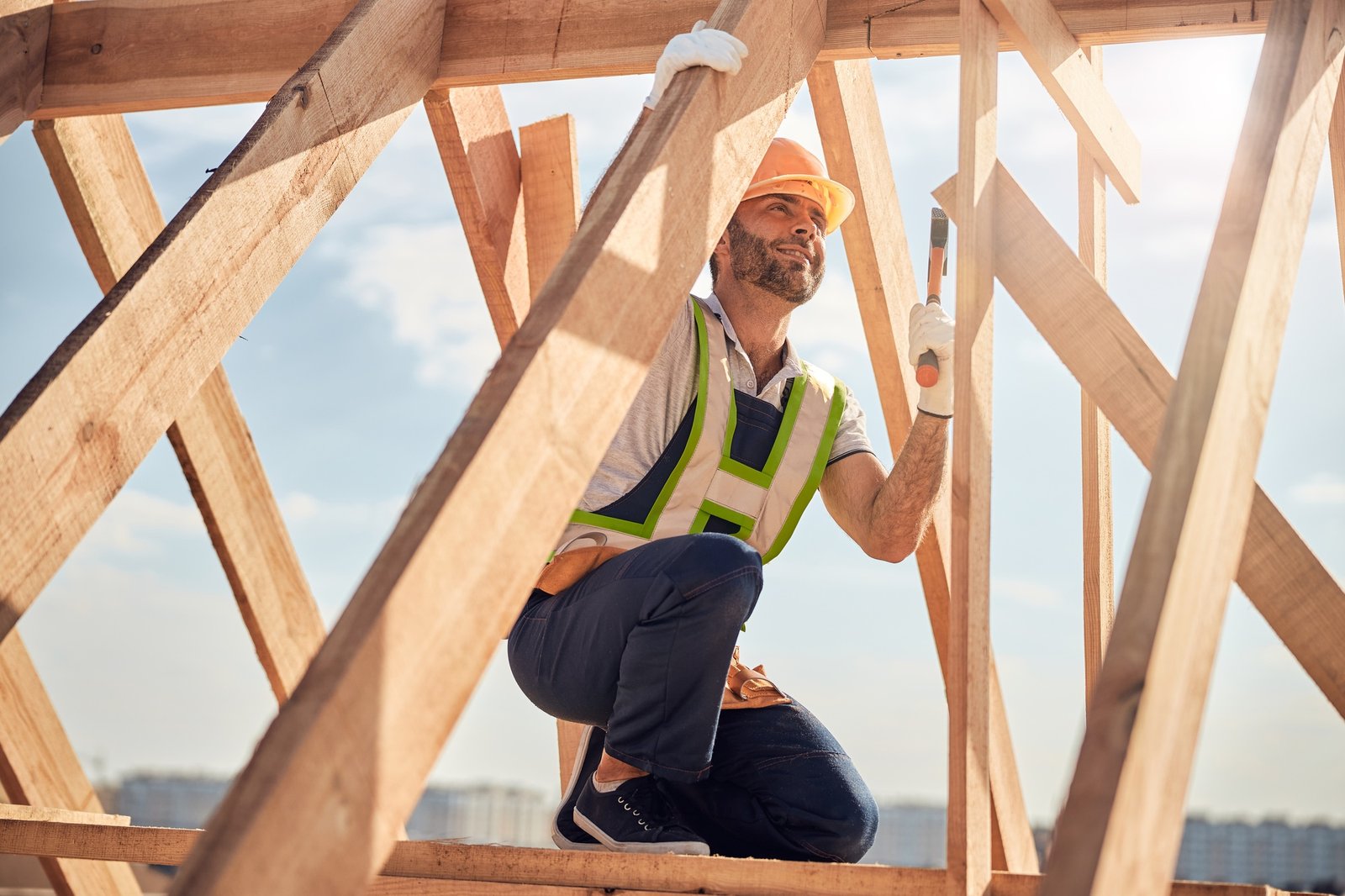 Joyous construction site worker with hammer building a roof carcass